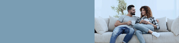 couple sitting on couch holding coffee mugs and smiling at one another